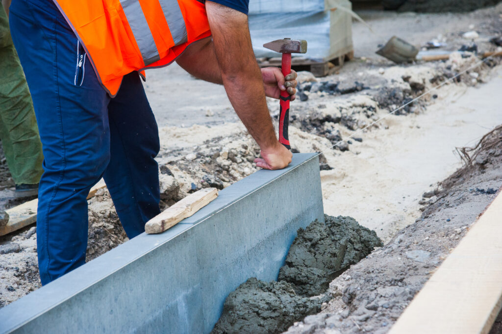 Darbuotojas ruošia pagrindą statyboms, formuojamas betono kraštas ir lyginamas paviršius sklype